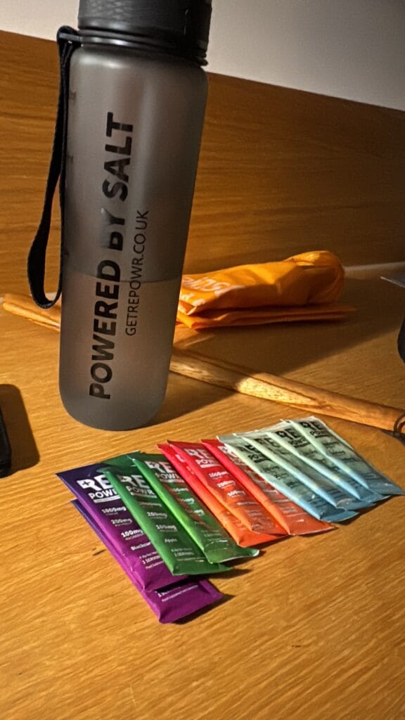 Electrolyte hydration sticks laid out on a hotel desk next to a reusable water bottle for travel and fitness use