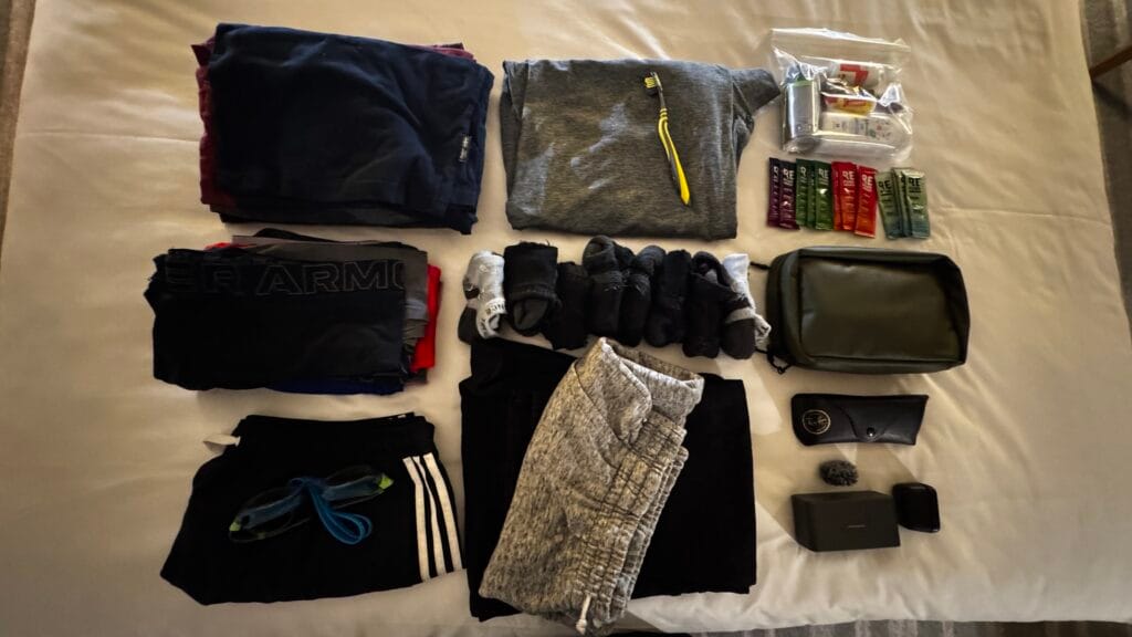 Minimalist travel packing layout on a hotel bed including clothes, toiletries, tech accessories, and essentials