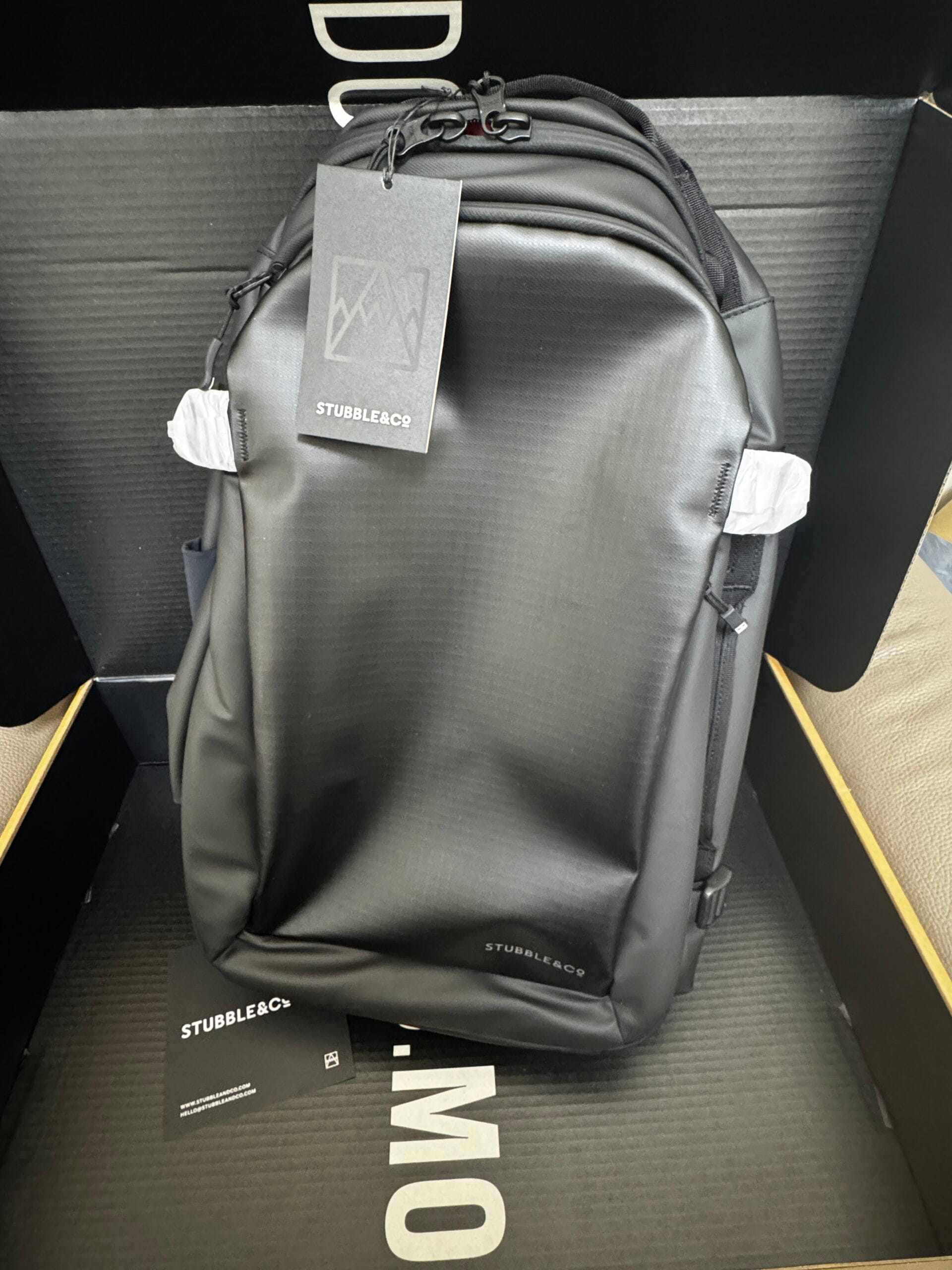 Front view of 30L black backpack inside the box with brand tag attached