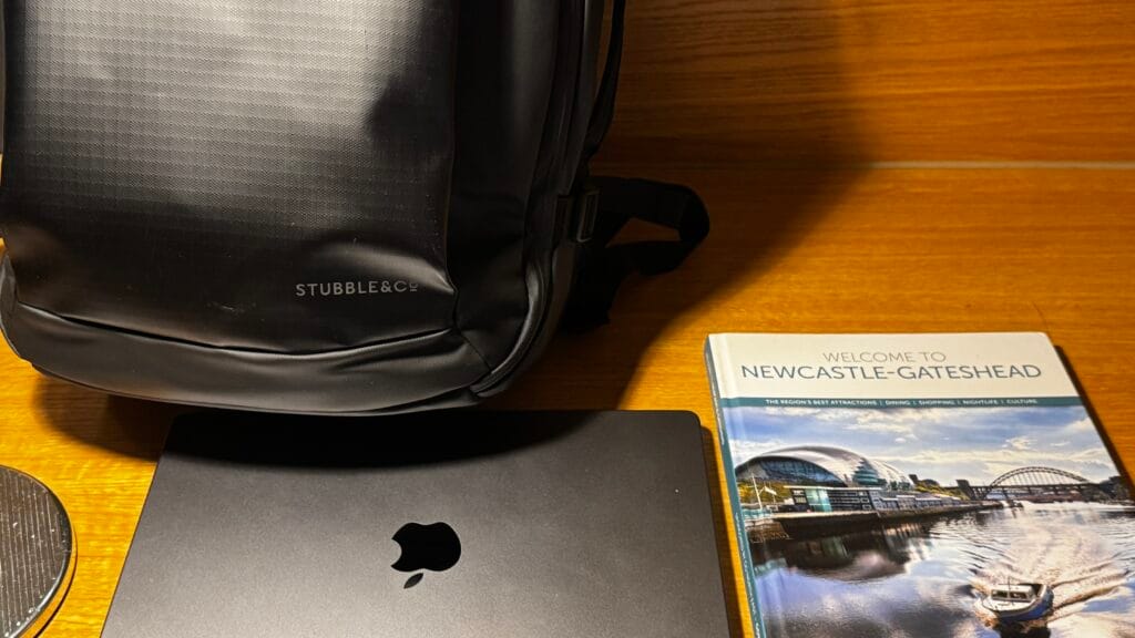 30L Hybrid backpack standing on a hotel desk next to a MacBook and a Newcastle Gateshead travel guide