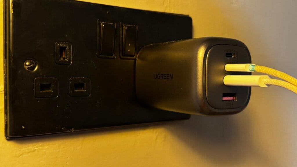 UGREEN GaN wall charger plugged into a black UK wall socket with two white USB-C cables connected