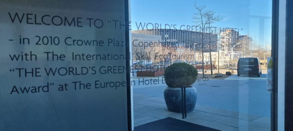 Crowne Plaza Copenhagen Towers window etched with the 2010 World's Greenest Hotel Skål EcoTourism Award text, Royal Arena visible through the glass