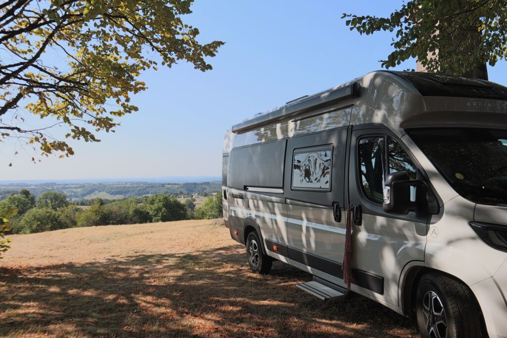 Camper van parked under a tree overlooking rolling countryside