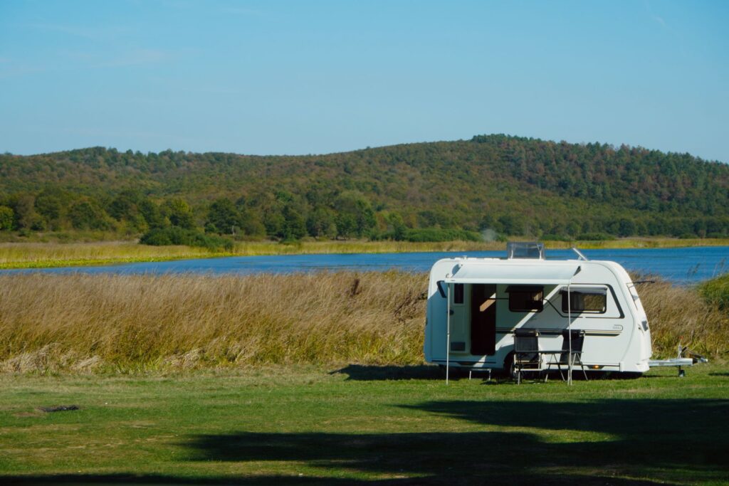Caravan pitched by a lake with its awning out and chairs set up